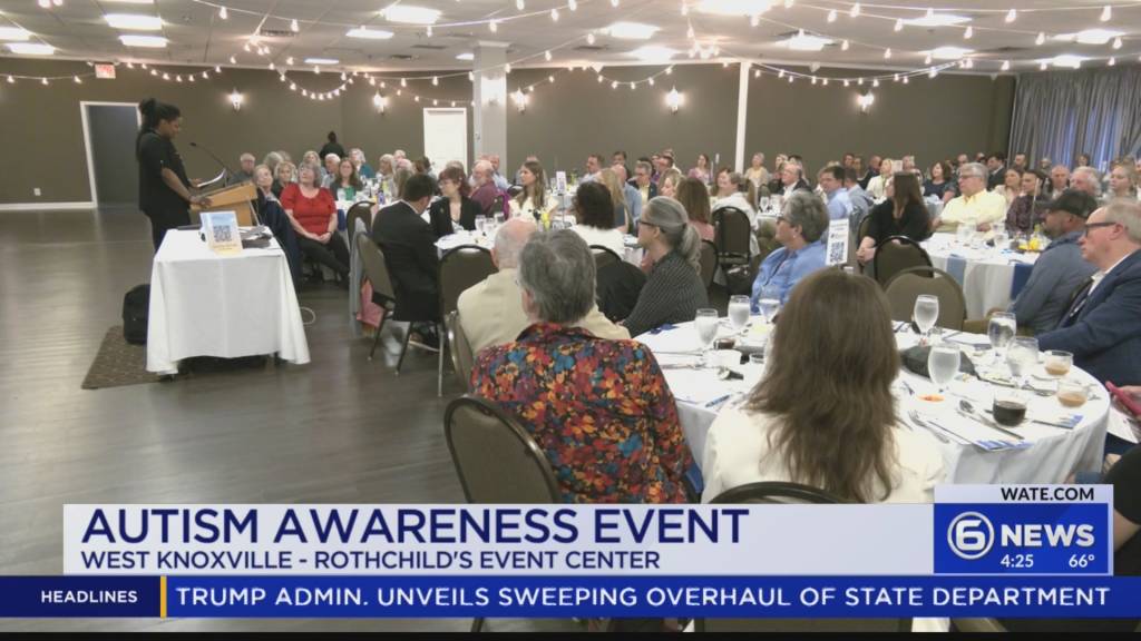 Speaker at a podium addresses a large audience at an Autism Awareness Event in a banquet hall.