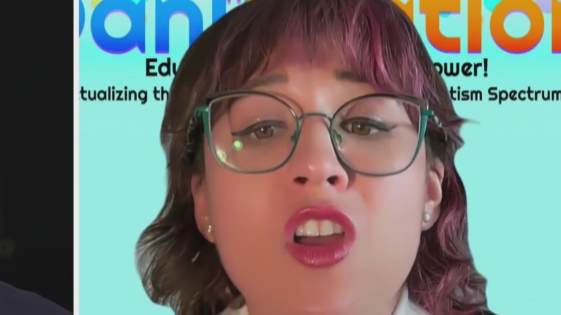 Close-up of a woman wearing green-framed glasses, speaking with her mouth open, against a turquoise background with colorful 'Education' text partly visible.